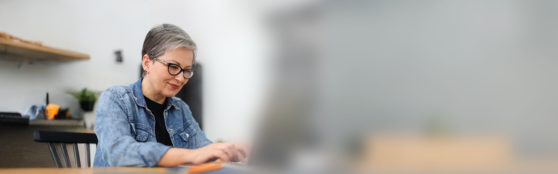 eine Frau sitzt an einem Tisch mit einem Laptop vor orangenem Hintergrund