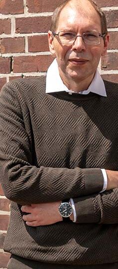 Der erfolgreiche Umschüler André Pardun steht mit verschränkten Armen vor einer geziegelten Hauswand.